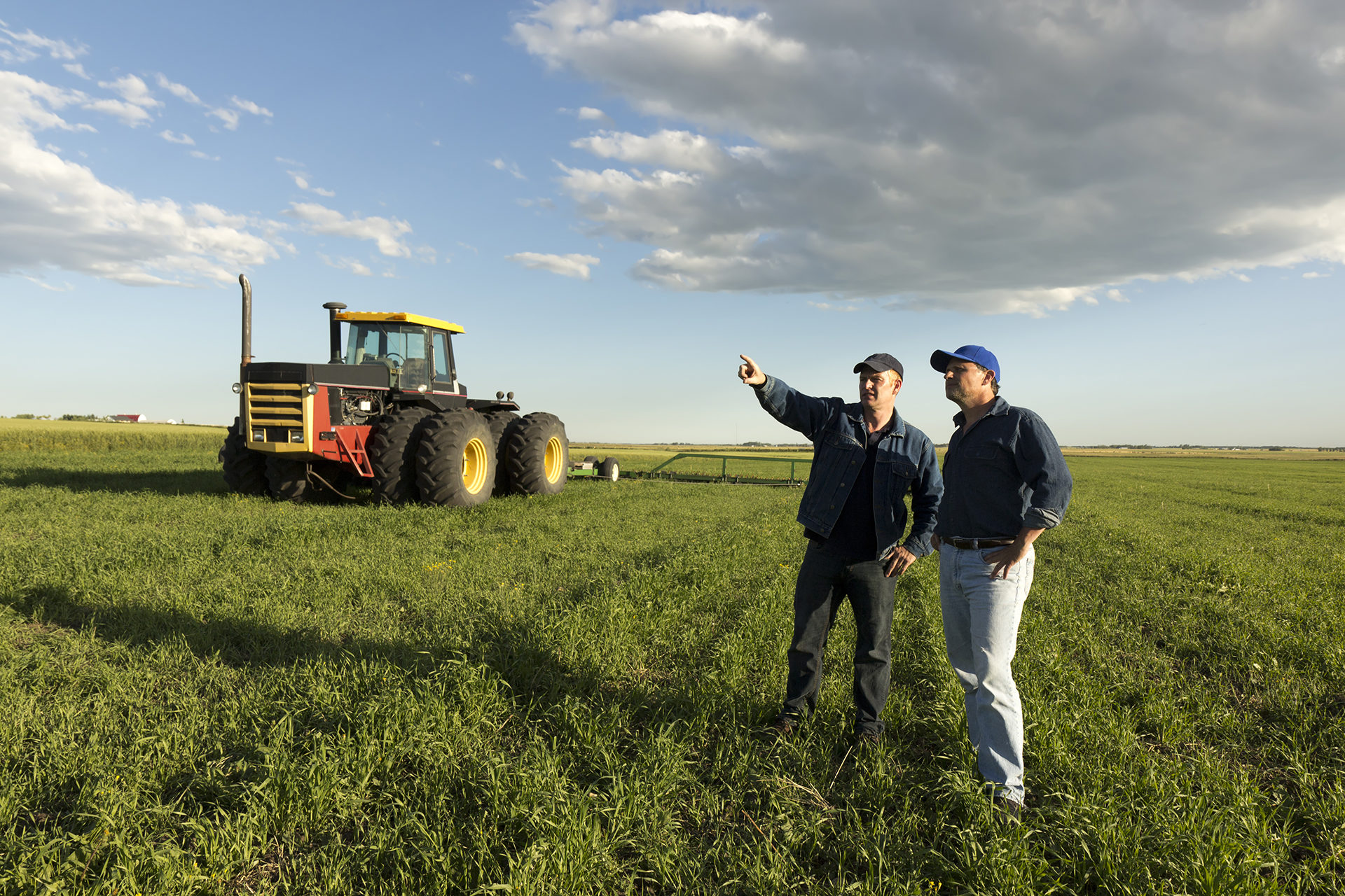 Two farmers in conversation in a field in front of a tractor.